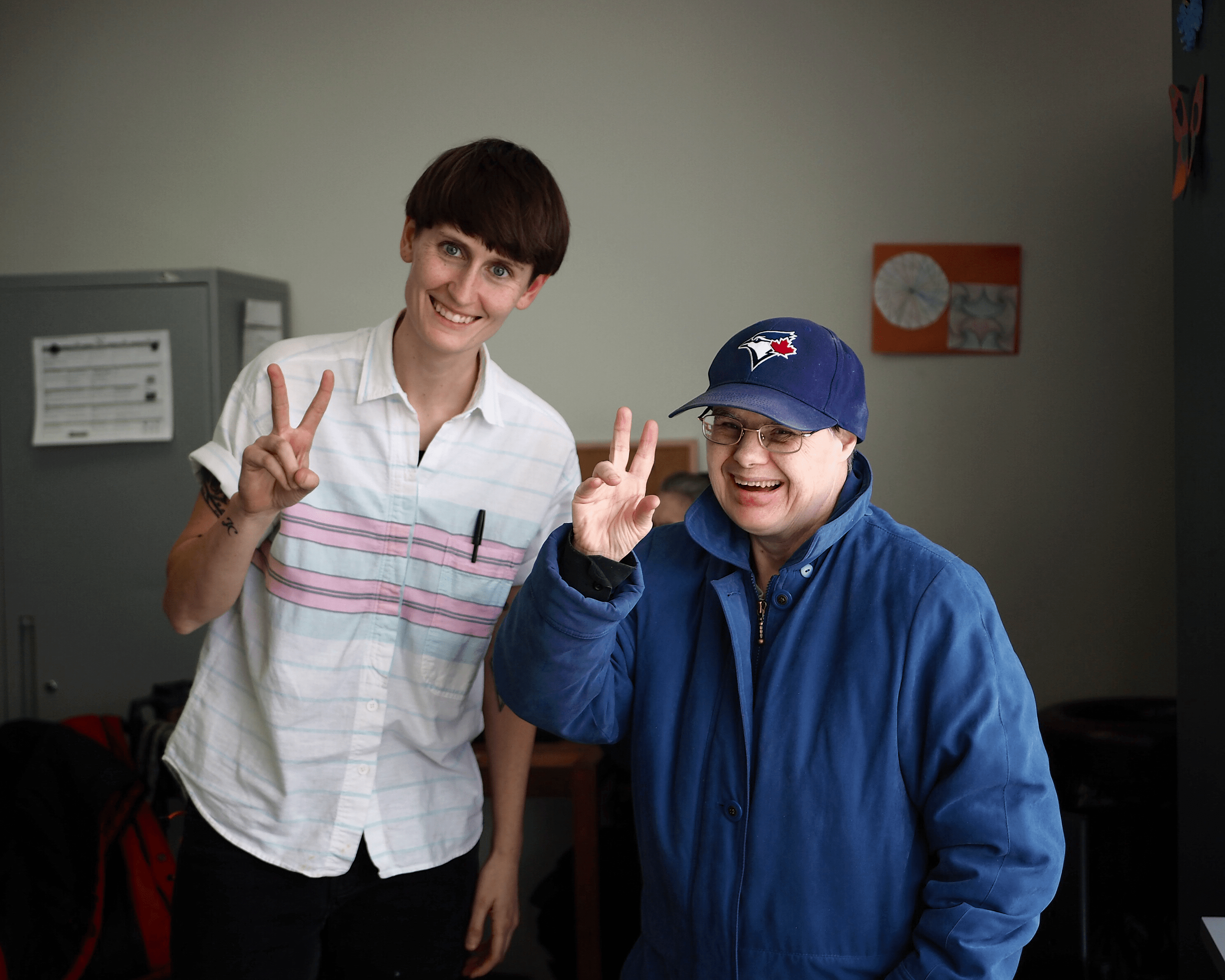 Two people are standing beside each other smiling and making peace signs.
