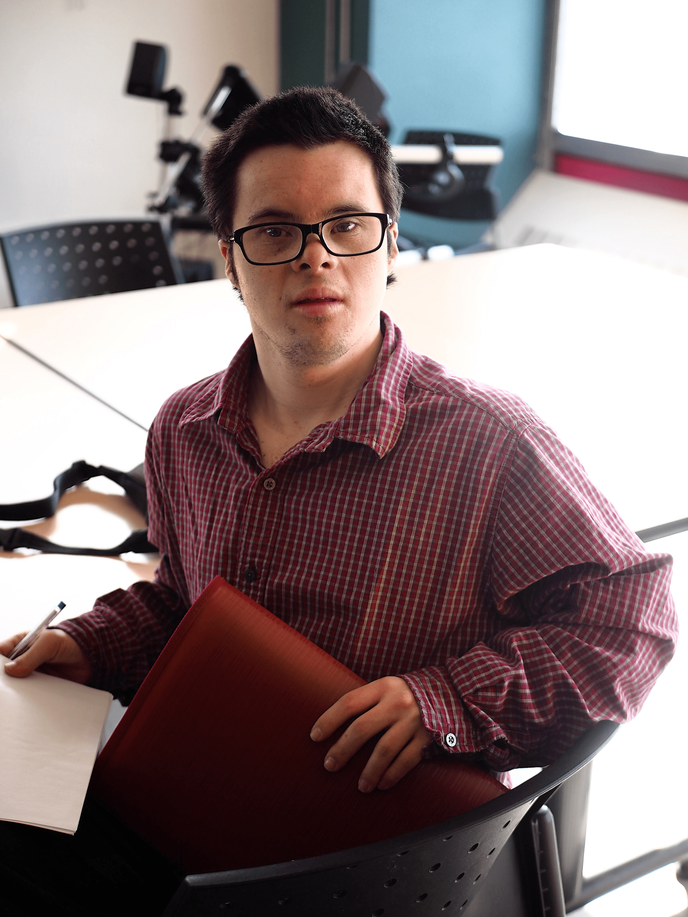 A man wearing glasses is looking at the camera. He is holding a binder.