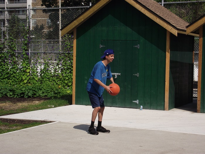 A man is outside holding a basketball. There is a green shed in the background.